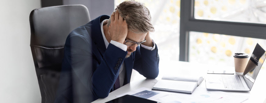 Stressed Mature Businessman In Suit Touching Head While Sitting At His Desk